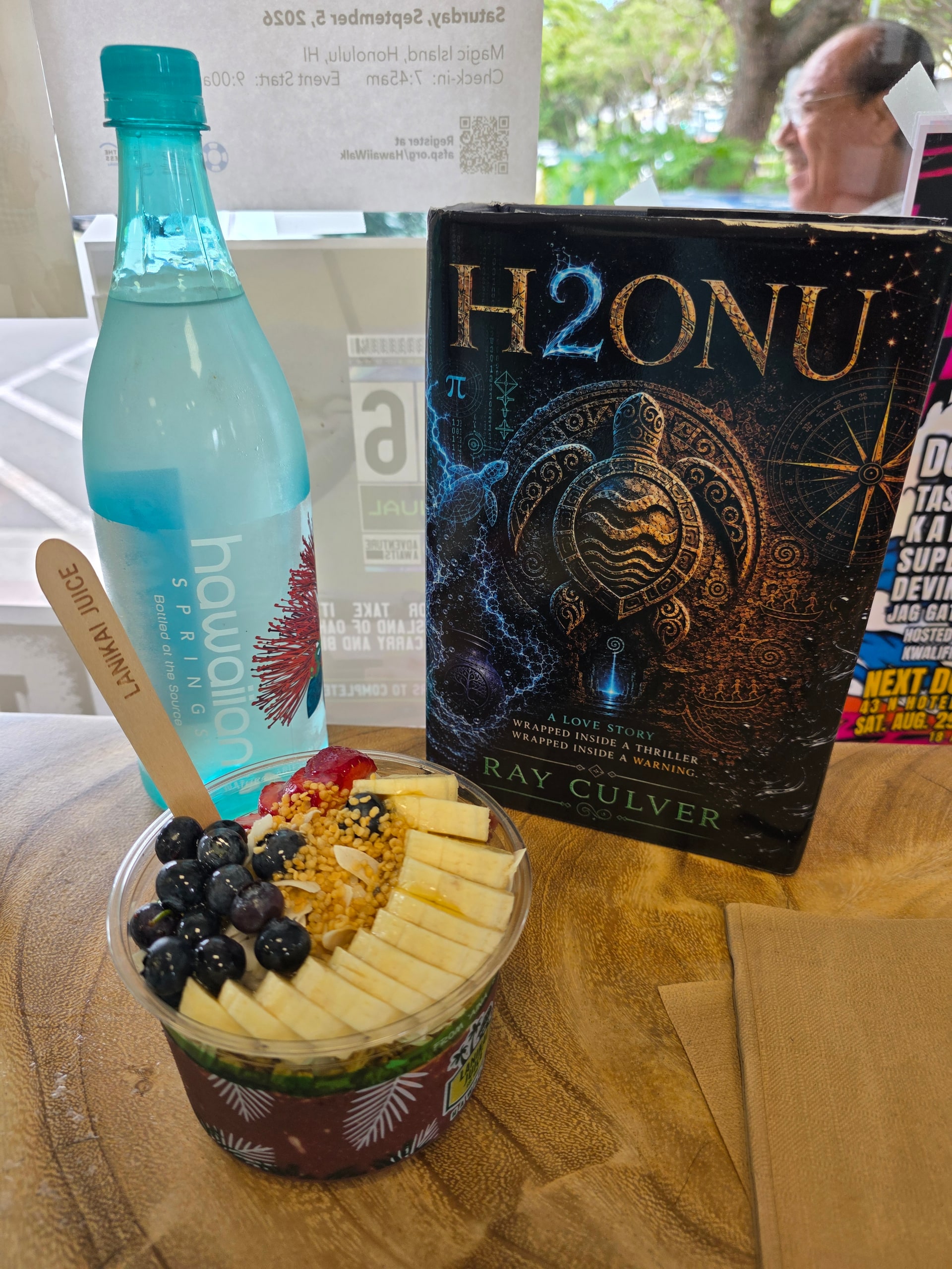 The H2ONU book beside Hawaiian Spring water and an açaí bowl at a café